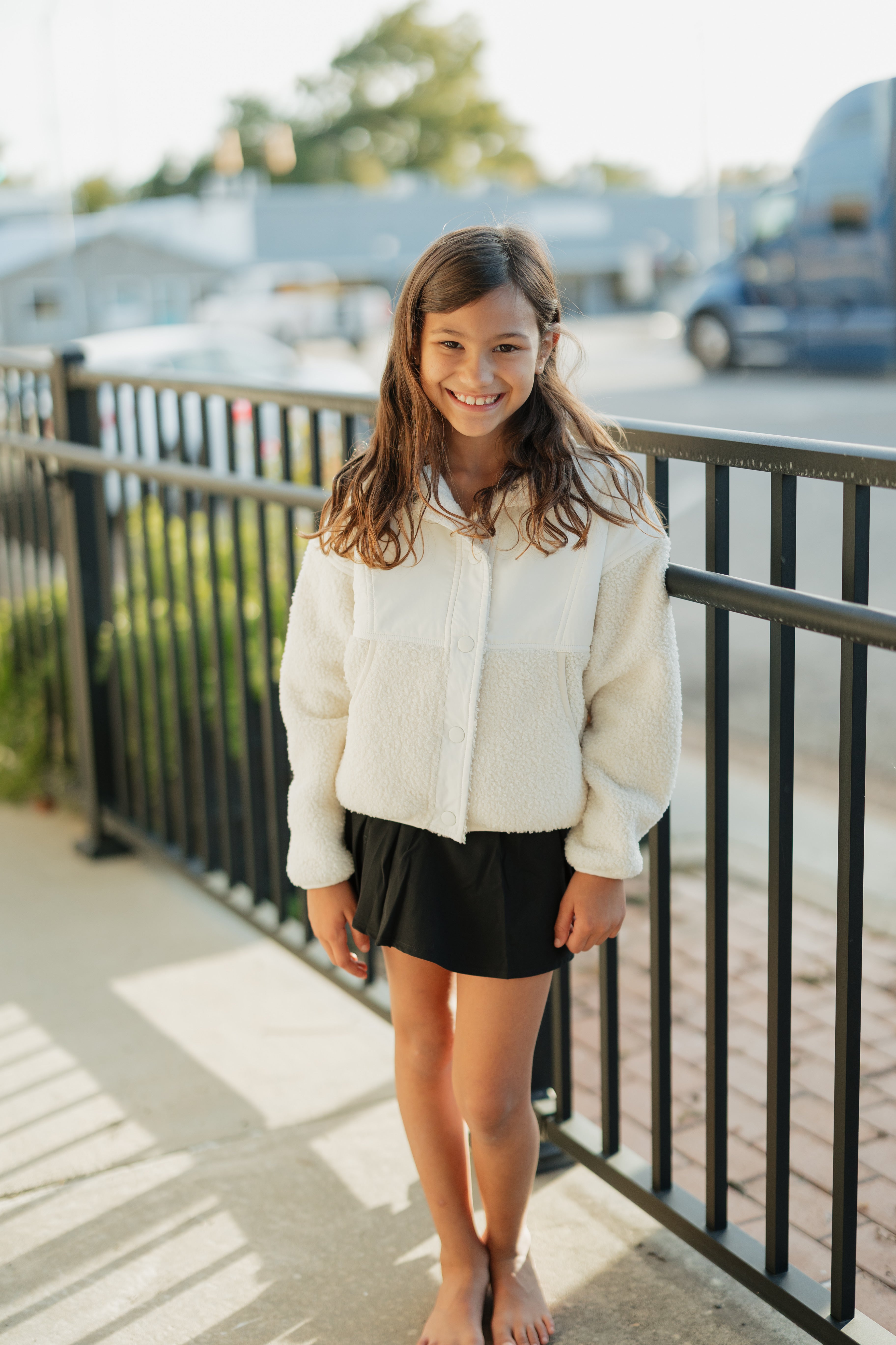 Young girl standing on a sidewalk wearing a white shirt and black skirt.