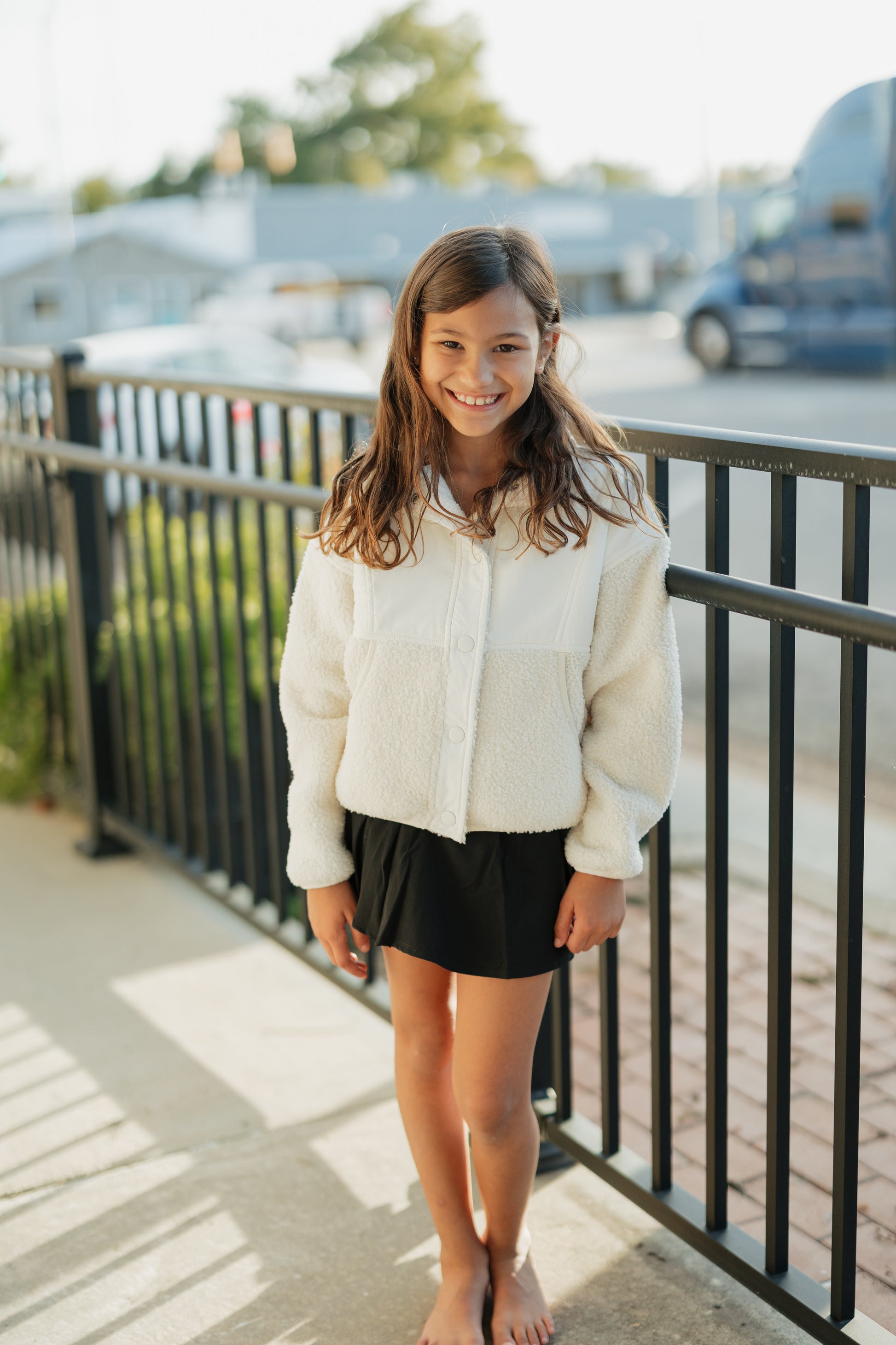 Young girl standing on a sidewalk wearing a white shirt and black skirt.