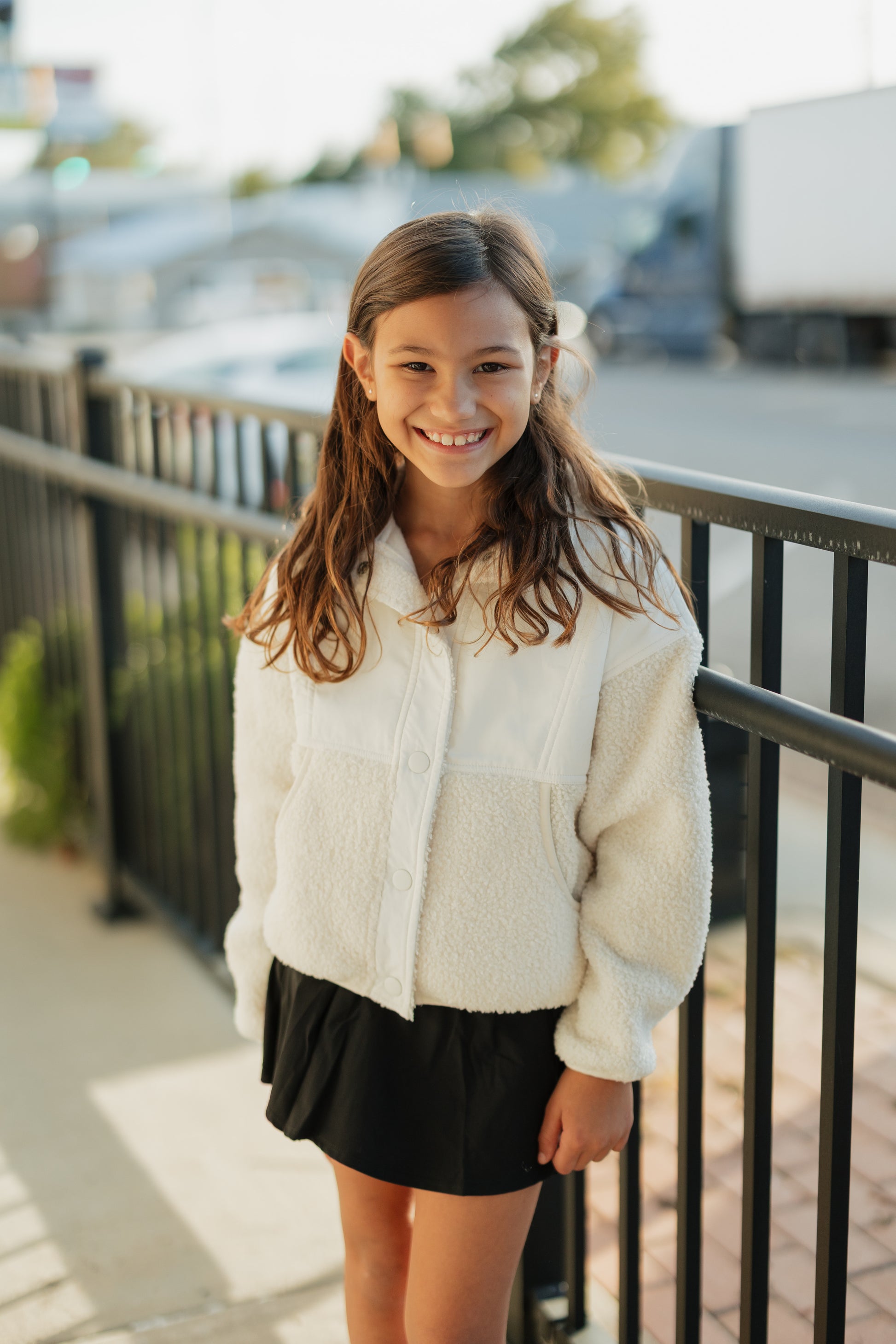 Young girl wearing a white fleece jacket and black skirt standing on a bridge.