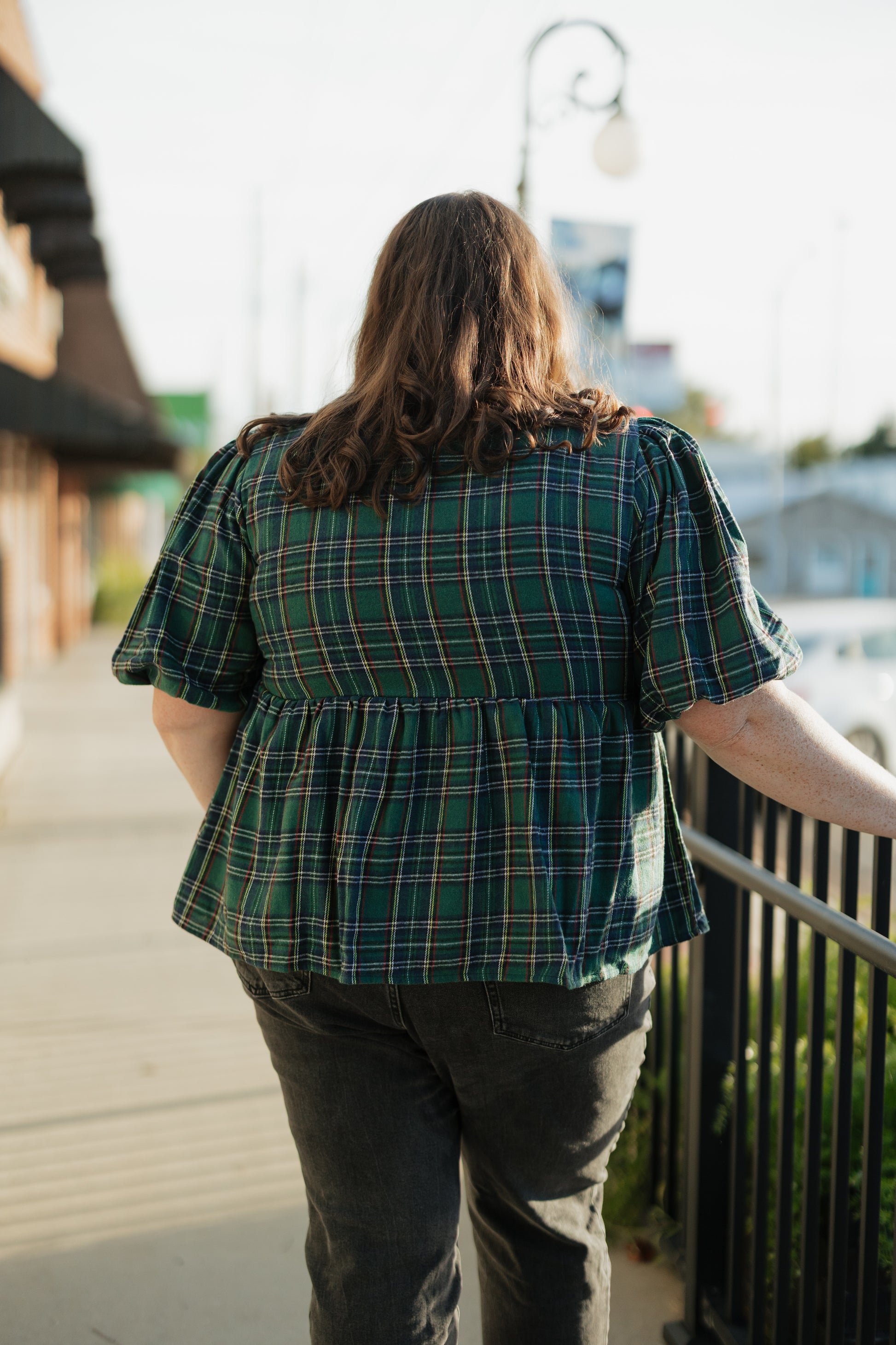 Person wearing a green plaid shirt walking on a sidewalk.