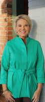 Woman wearing a green jacket standing against a brick wall.