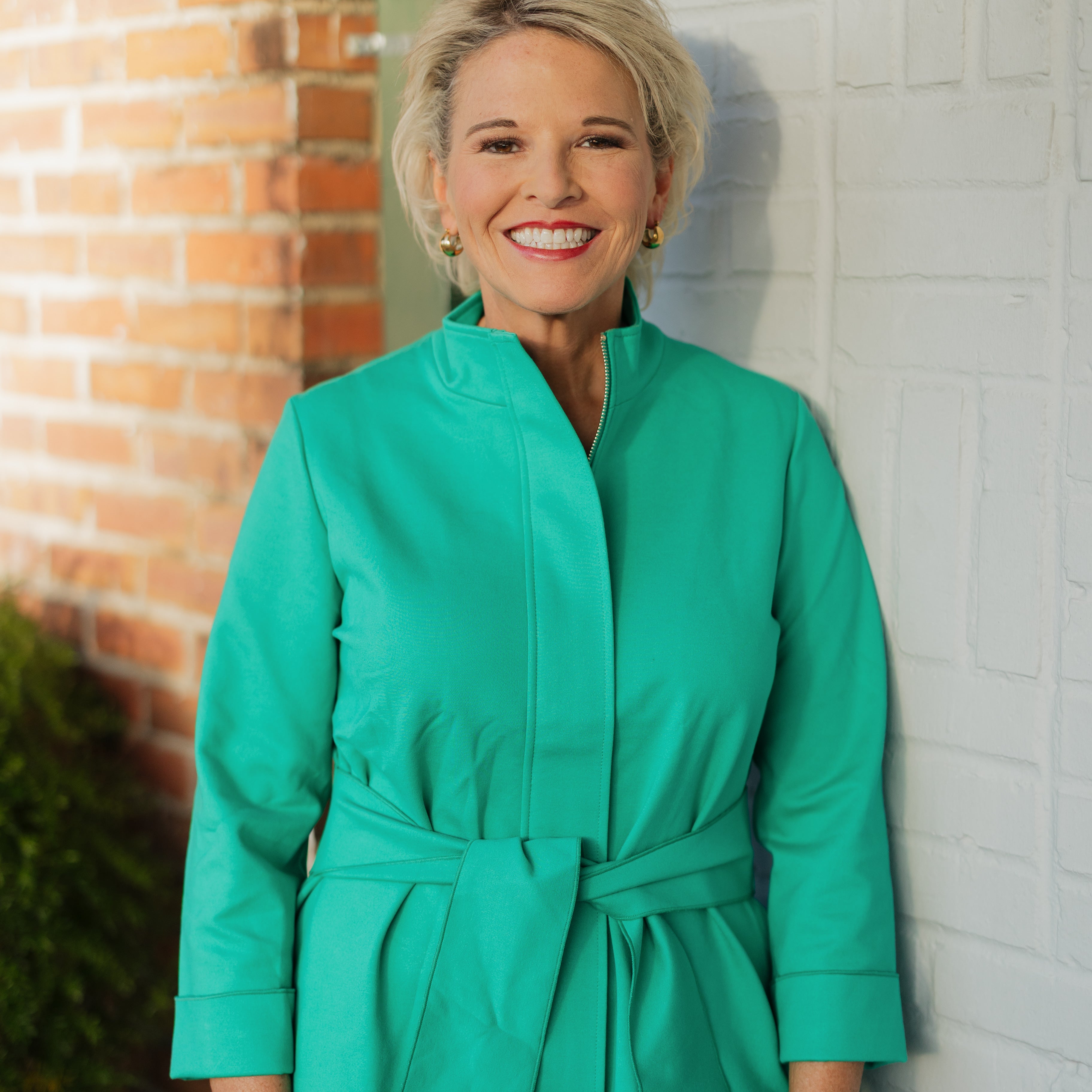 Woman wearing a green jacket standing against a brick wall.