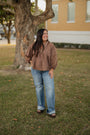 Woman standing outdoors in a grassy area with a tree and building in the background