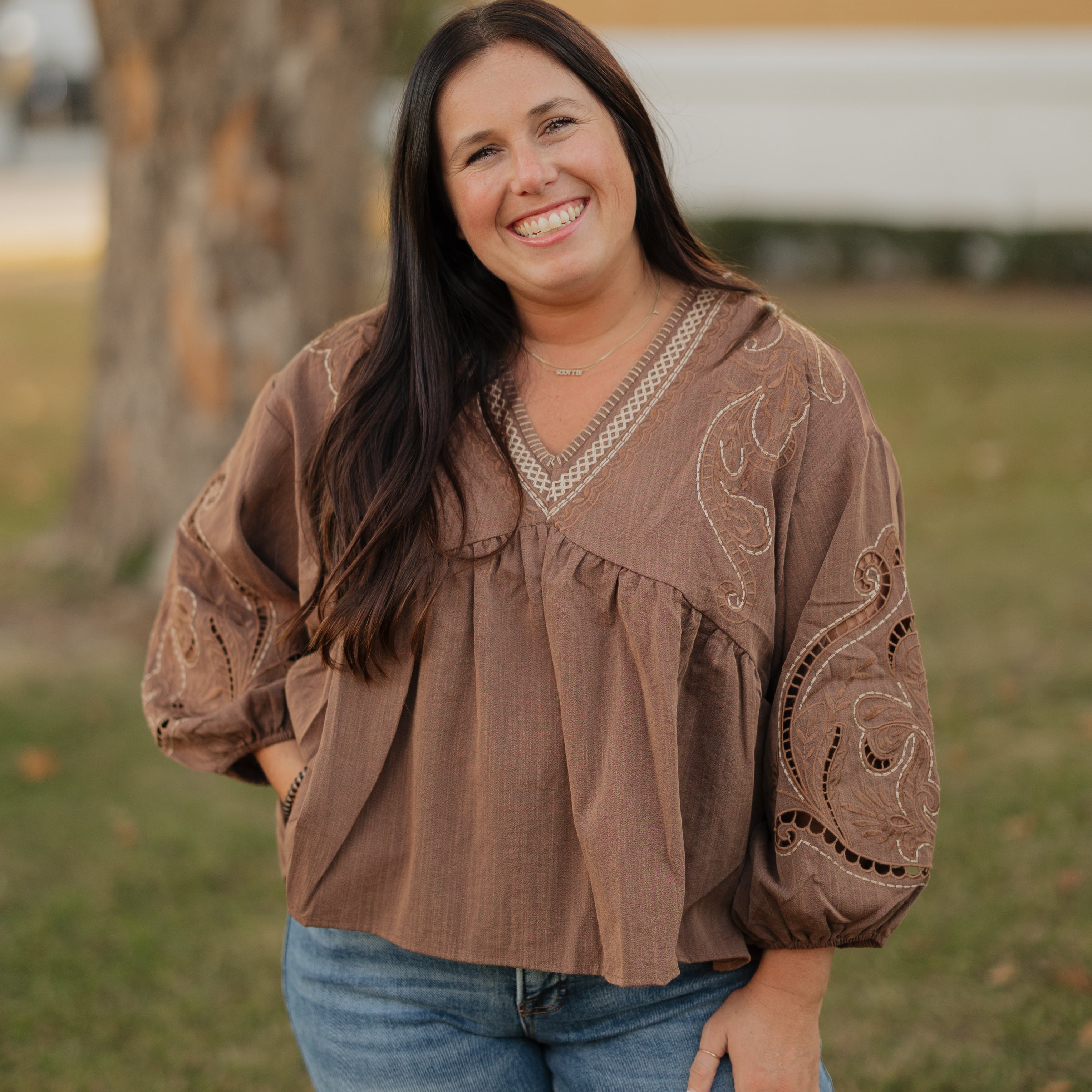 Woman wearing a brown blouse with intricate patterns outdoors