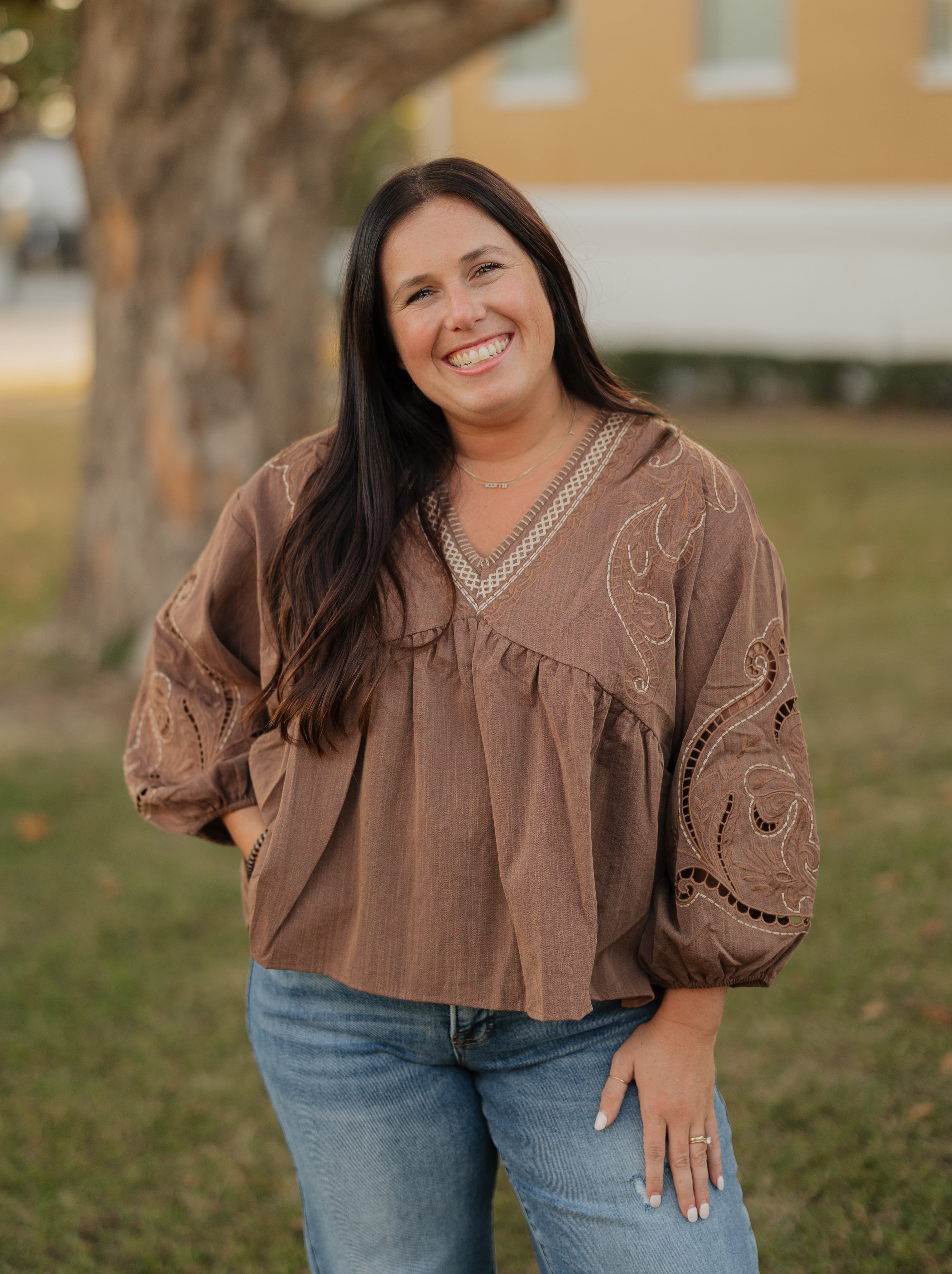 Woman wearing a brown blouse with intricate patterns outdoors