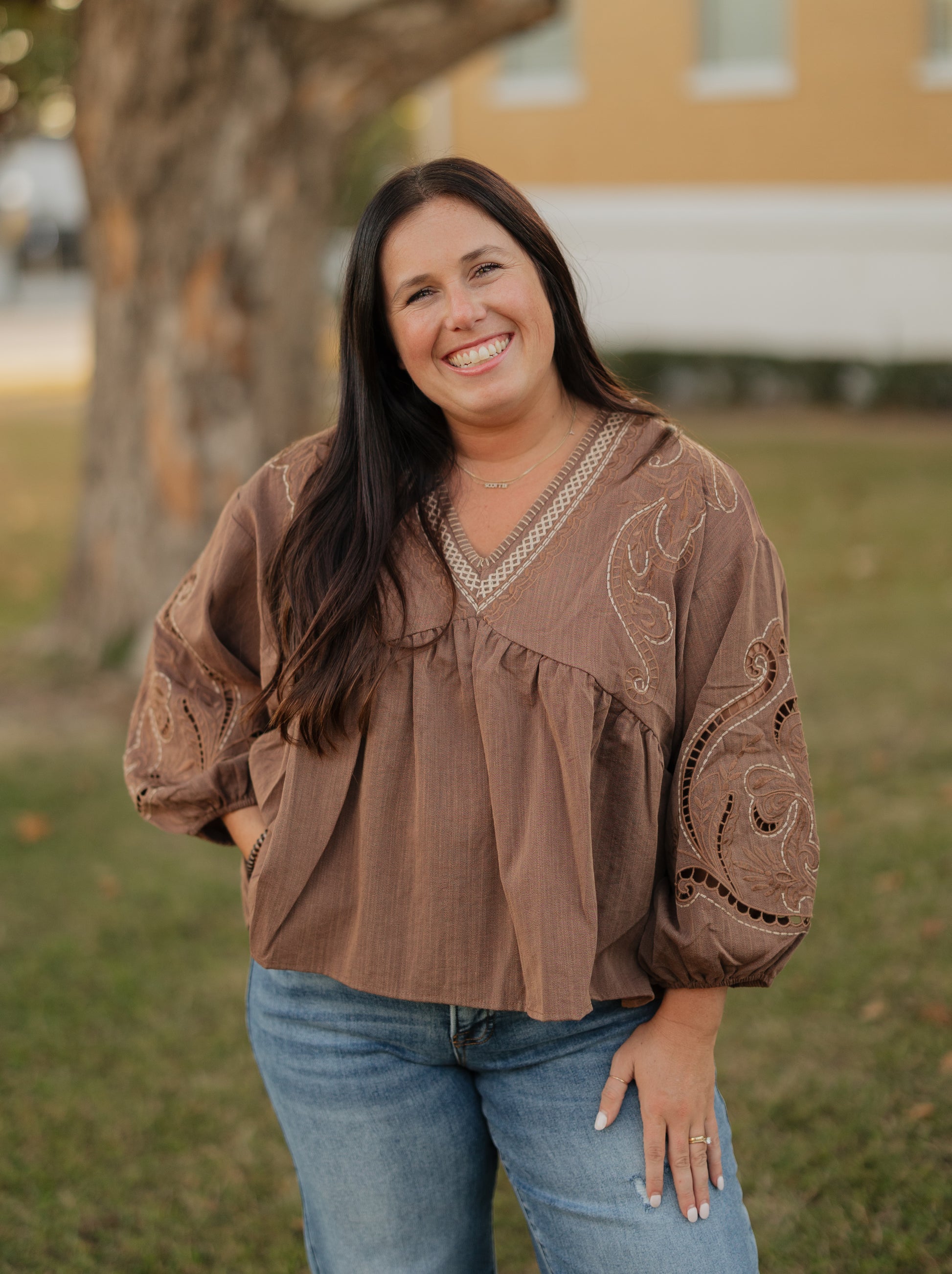 Woman wearing a brown blouse with intricate patterns outdoors