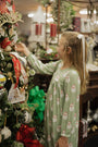 Young girl in a green pajama with Santa Claus patterns decorating a Christmas tree.