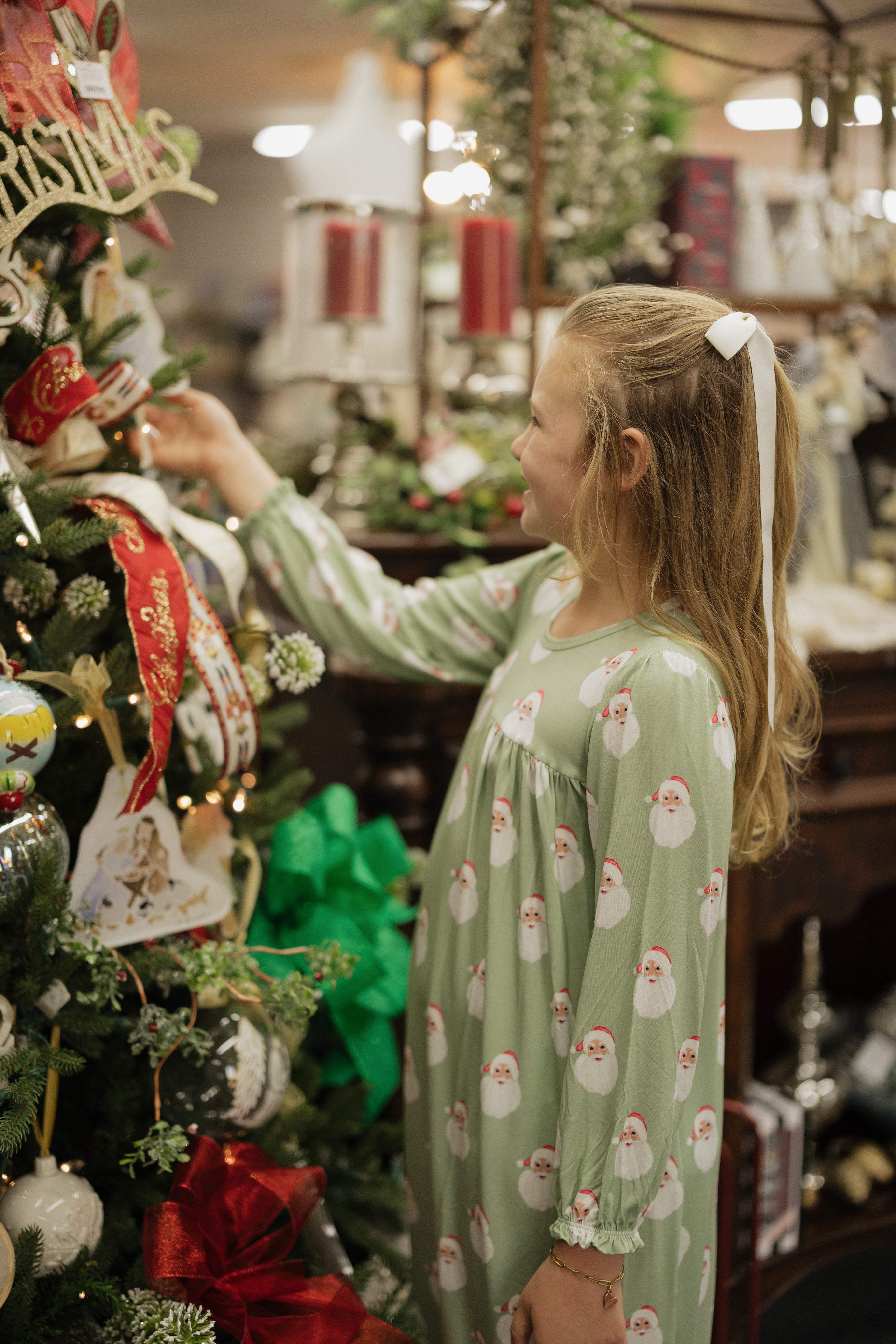 Young girl in a green pajama with Santa Claus patterns decorating a Christmas tree.