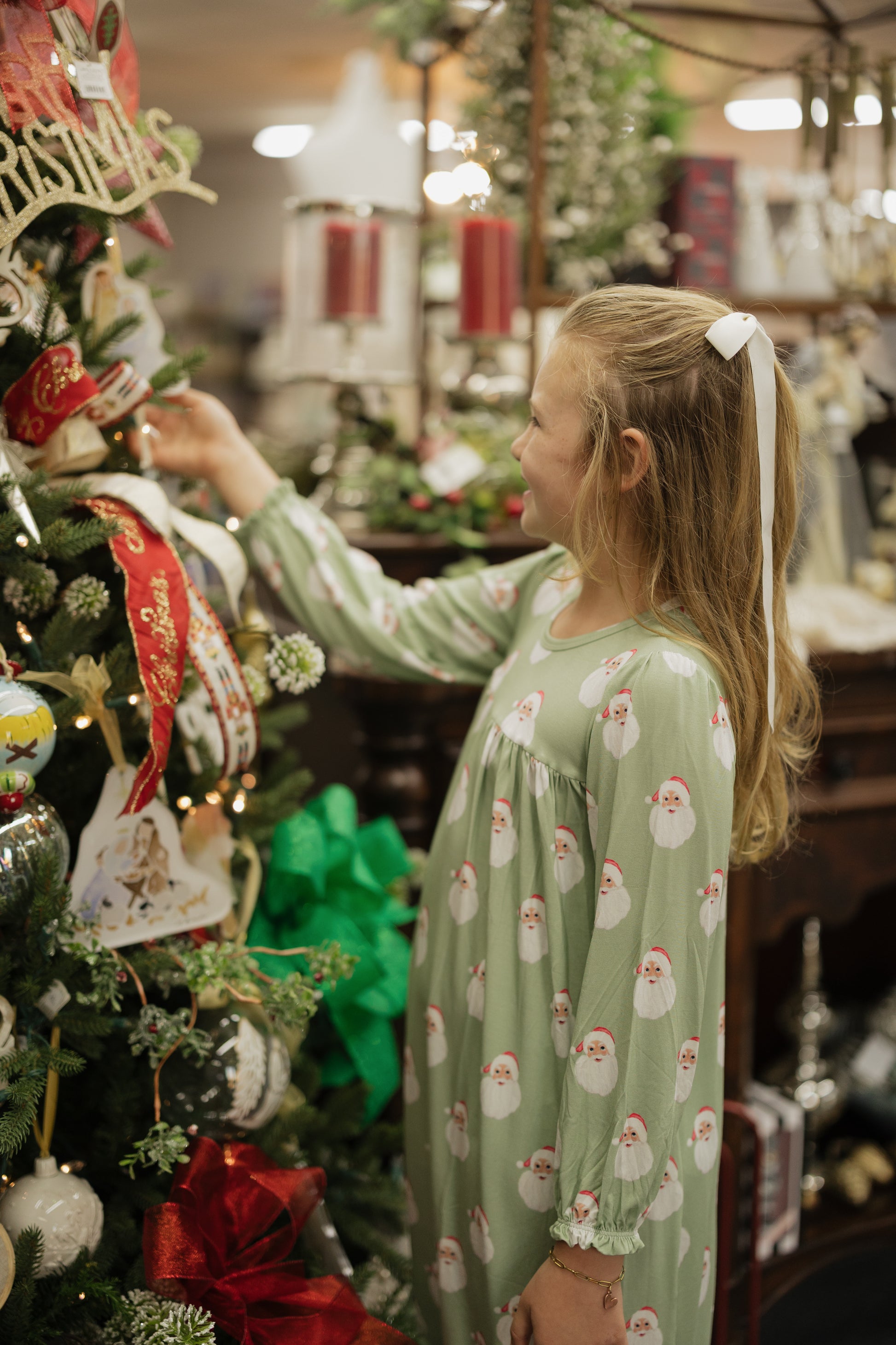 Young girl in a green pajama with Santa Claus patterns decorating a Christmas tree.
