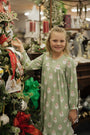 Young girl in a green nightgown with Santa Claus pattern standing next to a decorated Christmas tree.