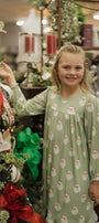 Young girl in a green nightgown with Santa Claus pattern standing next to a decorated Christmas tree.