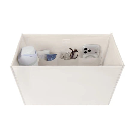 An off-white fabric organizer box with multiple interior compartments, shown holding various small items like a white bottle, a blue packet, eyeglasses, and a smartphone. The box is photographed on a seamless white background.
