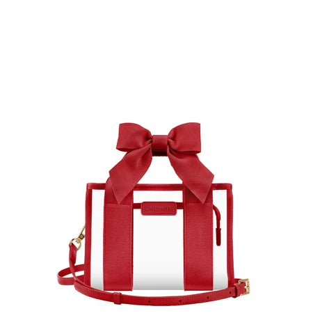 A red structured handbag with a large bow on top, clear front panels, a small front pouch, and a matching red shoulder strap on a plain white background.