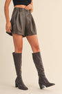 Person wearing brown leather shorts and knee-high boots on a beige background