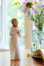 Wooden figurine of a woman holding flowers next to a vase with flowers on a table.