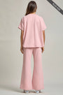 Woman wearing a pink outfit with wide-leg pants on a plain background