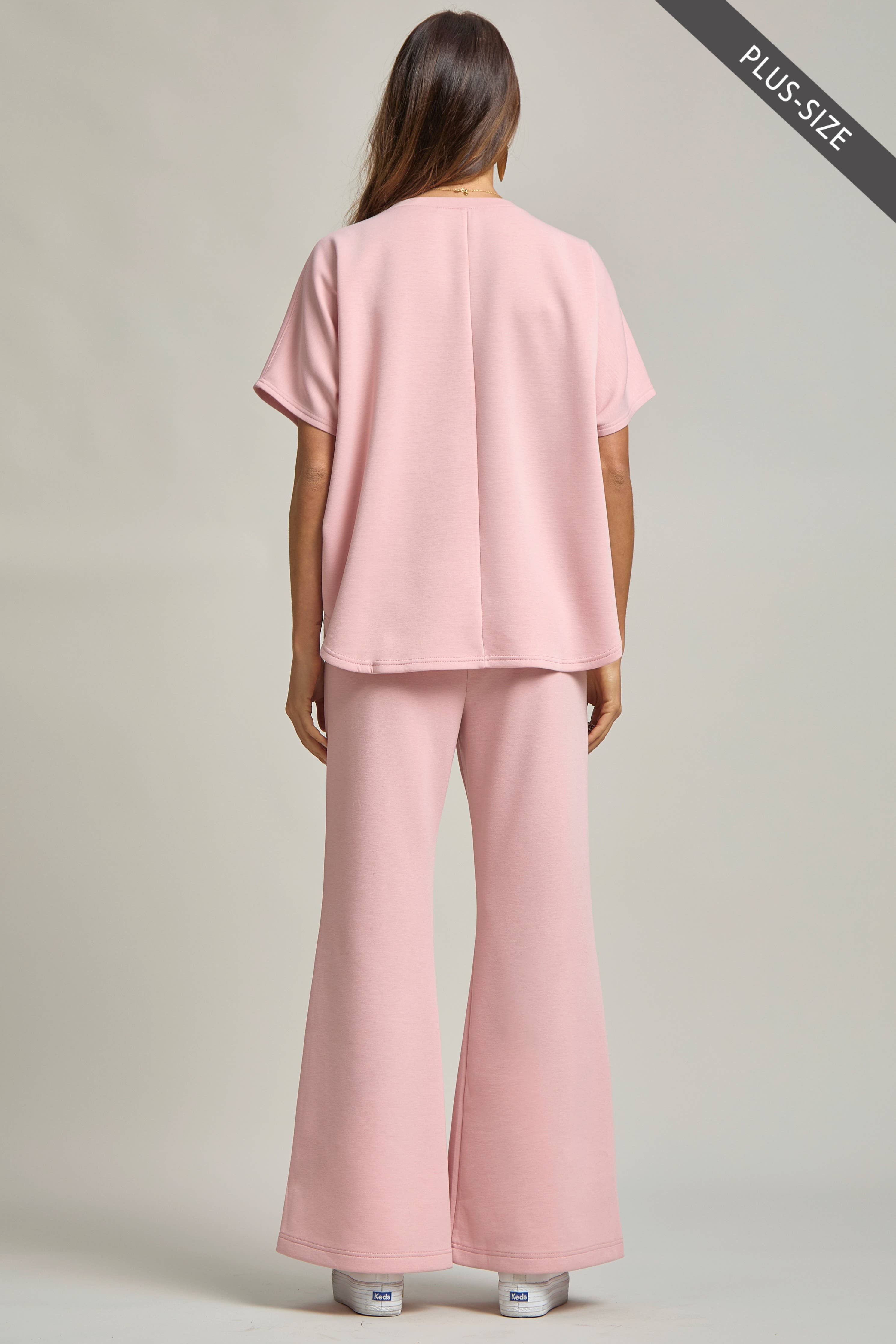 Woman wearing a pink outfit with wide-leg pants on a plain background