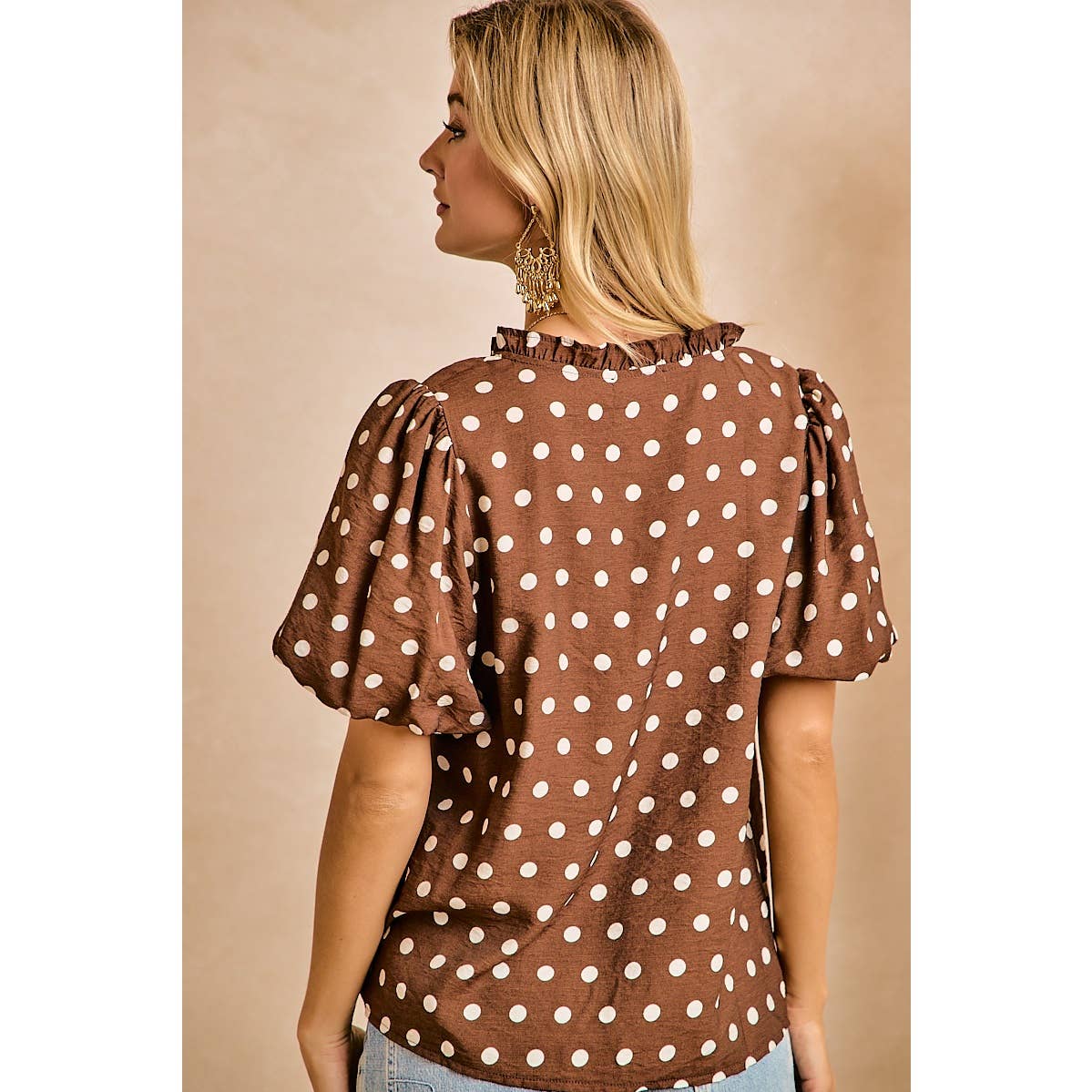 Woman wearing a brown blouse with white polka dots against a beige background