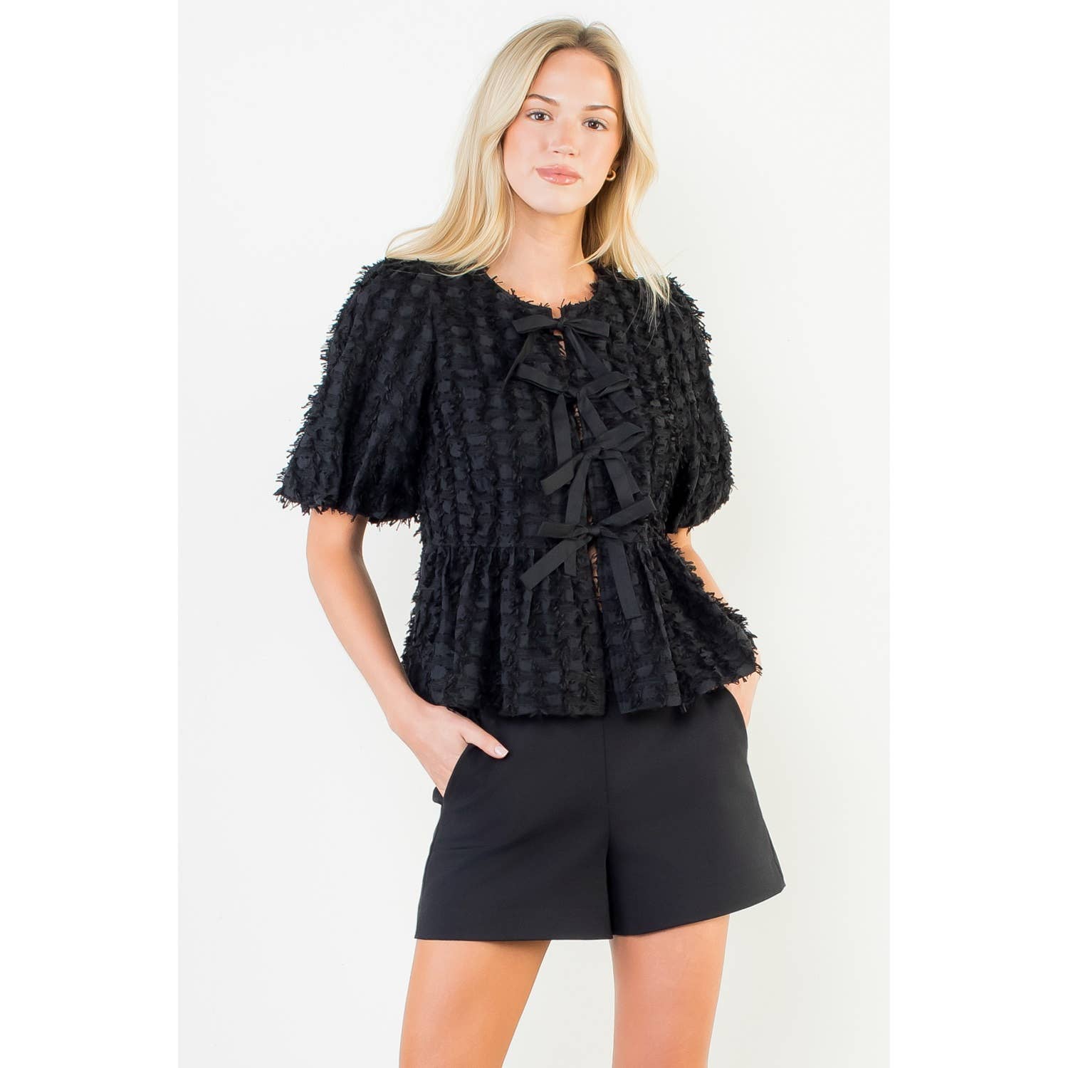 Woman wearing a black textured top and shorts on a white background