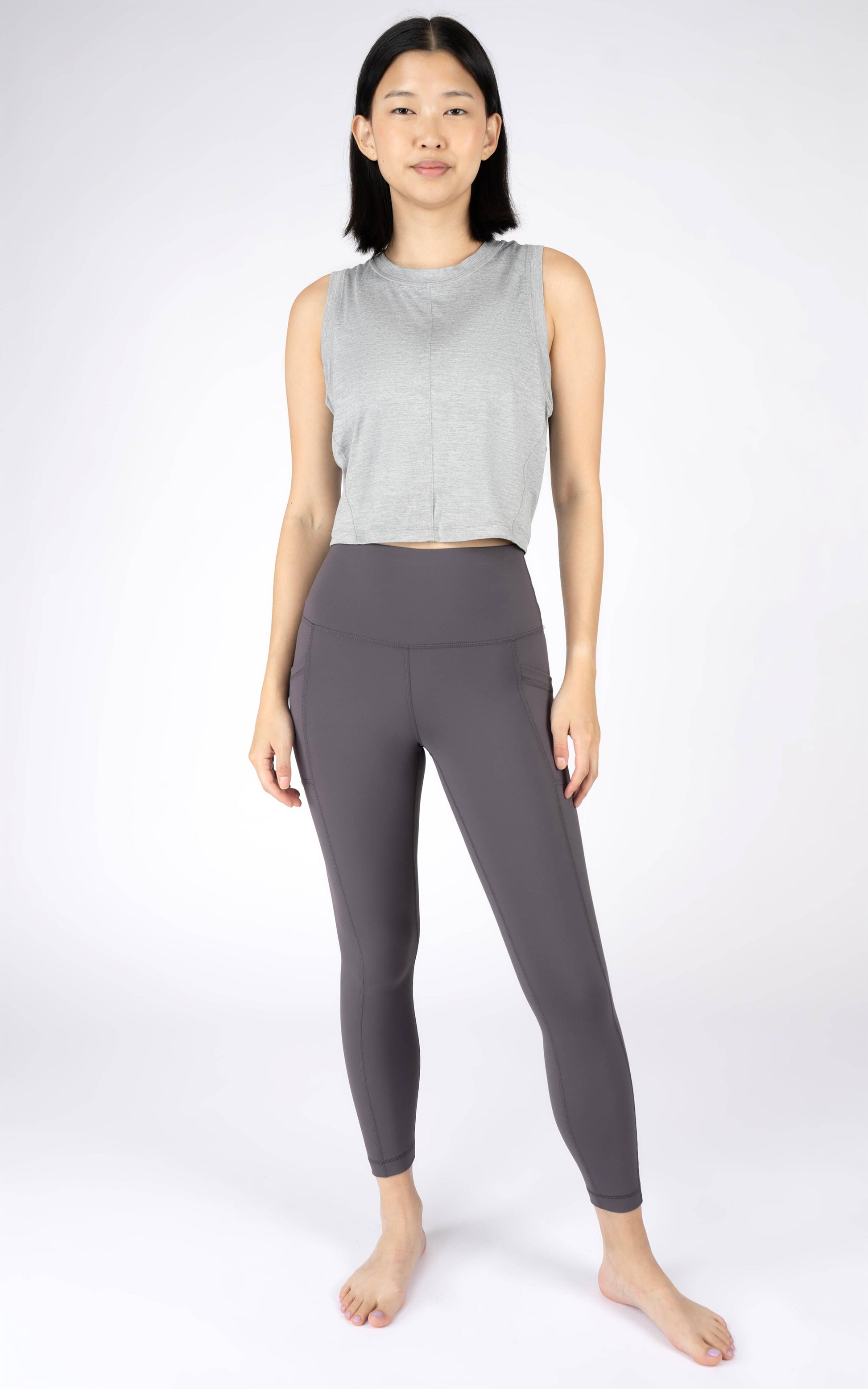 Woman wearing a gray sleeveless top and black leggings on a white background