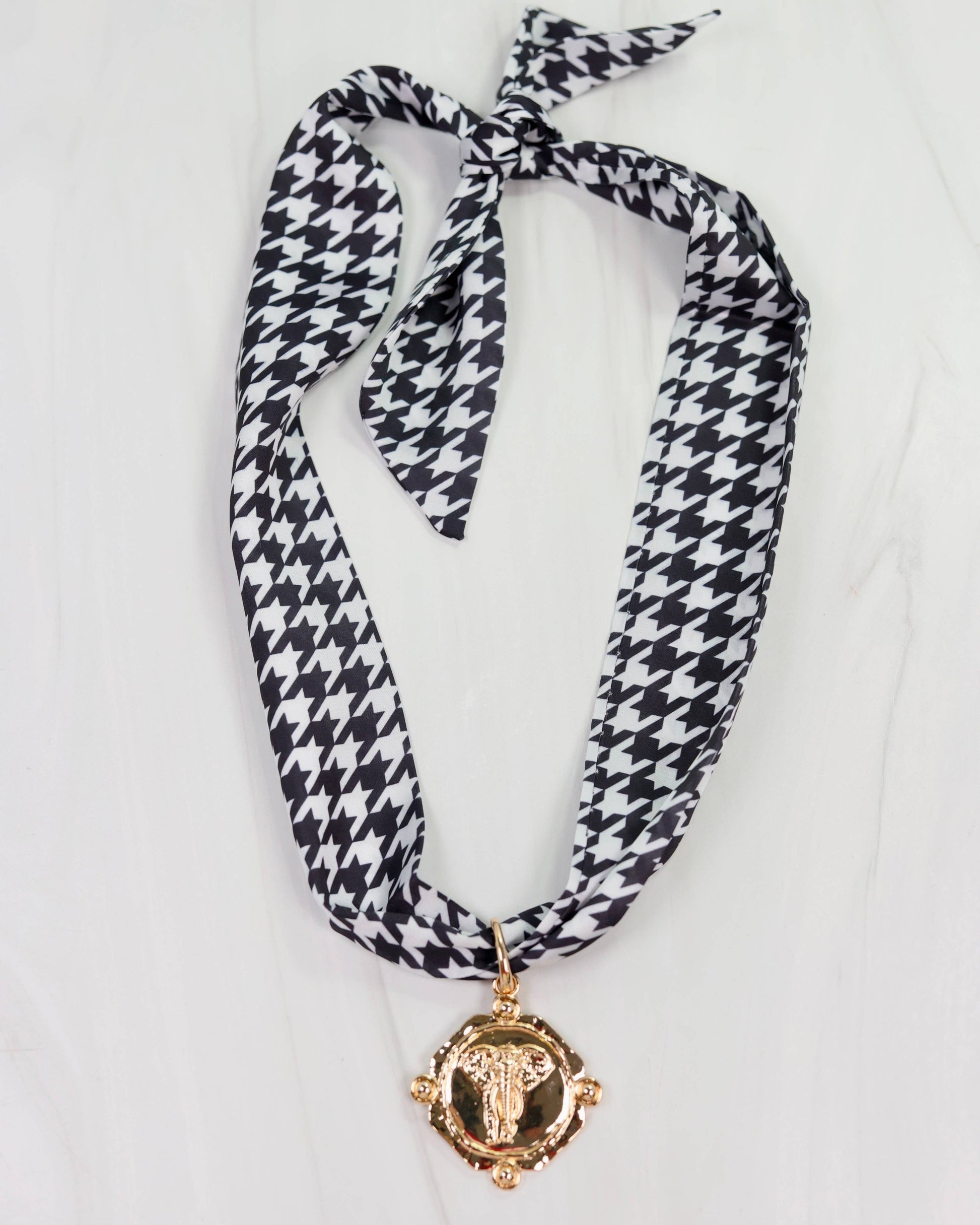 Houndstooth patterned scarf with a gold medallion on a white background