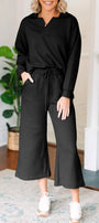 Woman wearing a black outfit in a home setting with a plant and fireplace in the background.