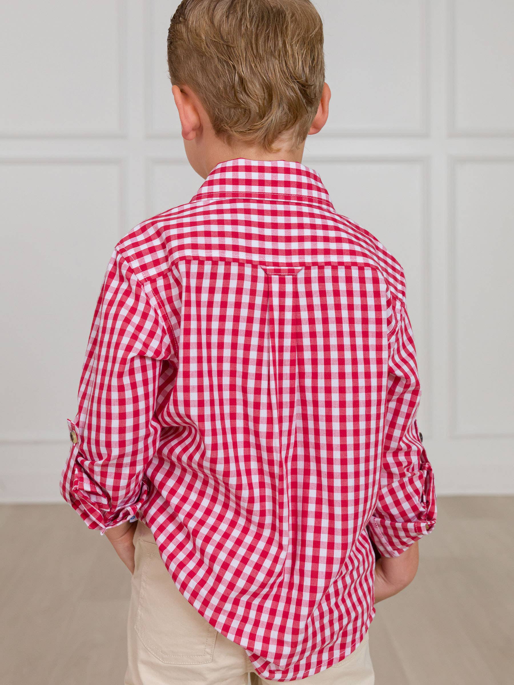 Child wearing a red and white checkered shirt with sleeves rolled up, standing against a neutral background.