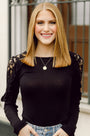 Woman wearing a black top with lace sleeves and a necklace, standing outdoors.