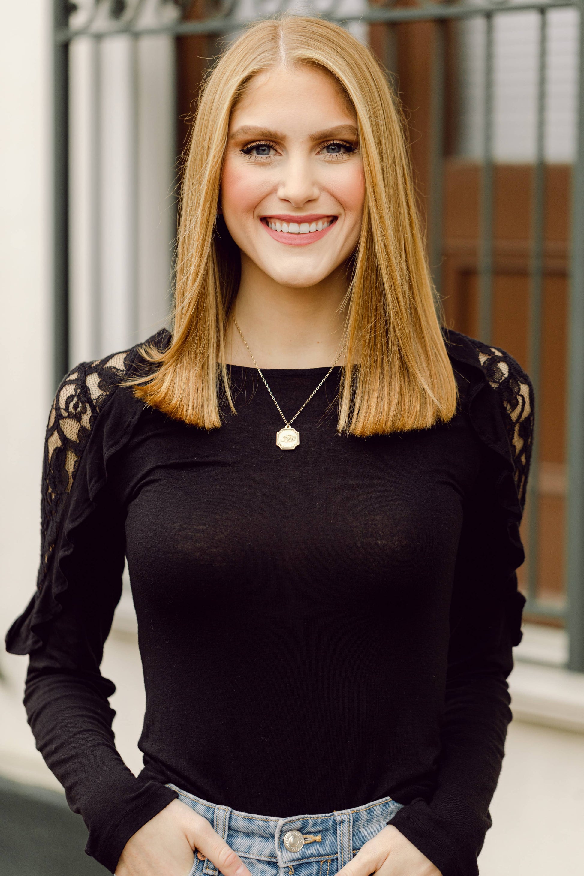 Woman wearing a black top with lace sleeves and a necklace, standing outdoors.