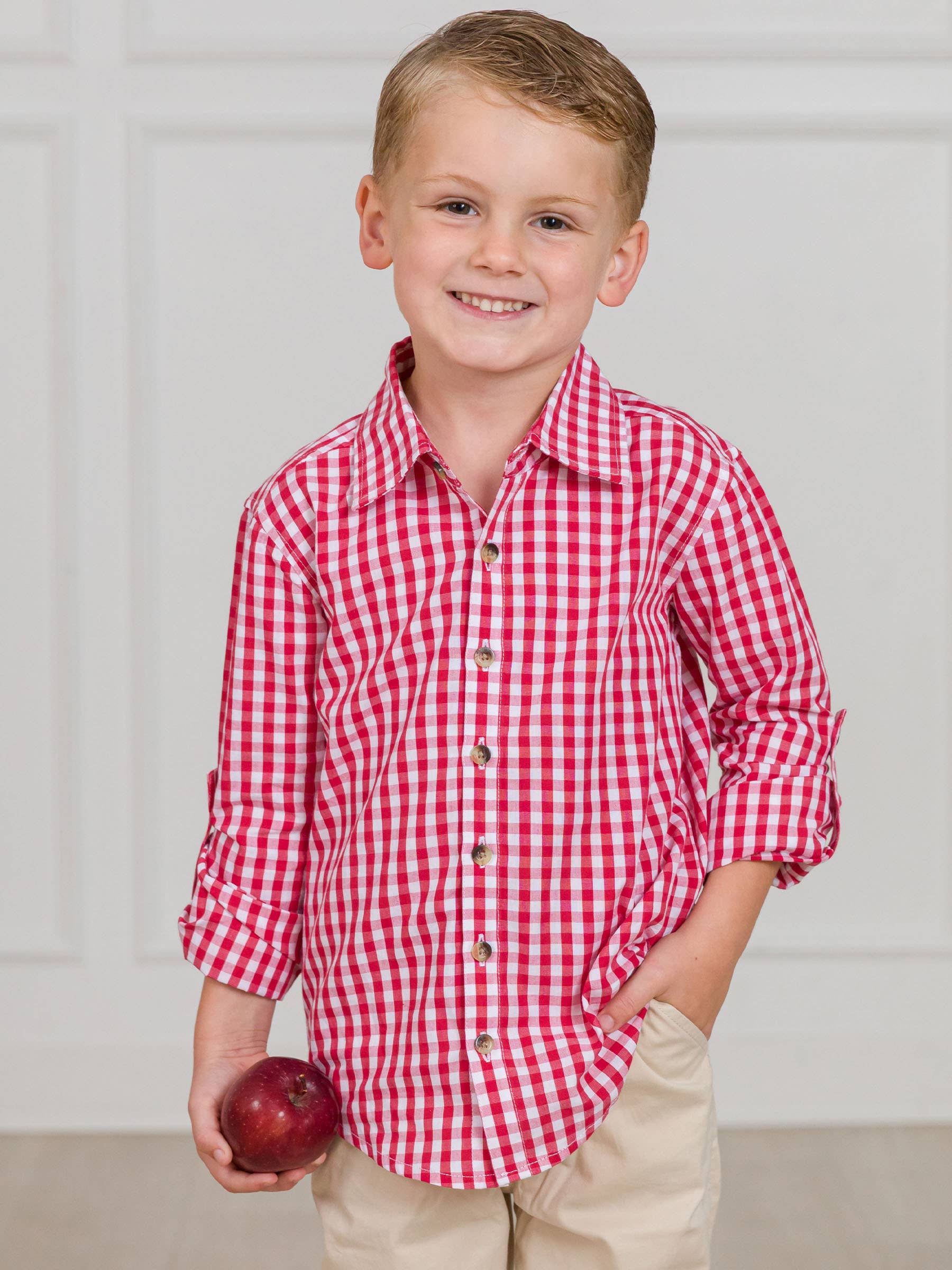 Young boy wearing a red and white checkered shirt holding an apple against a plain background