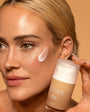 Woman applying a tan product to her face with a tan-colored background