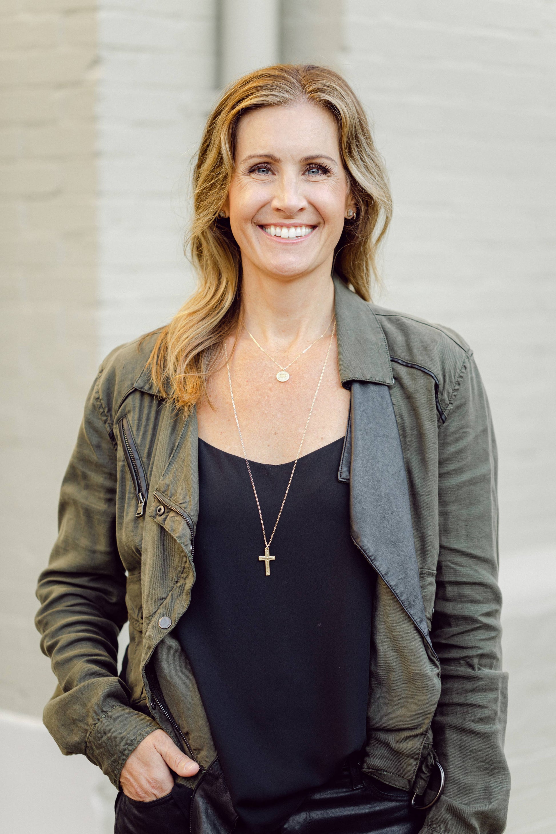 Woman wearing a green jacket and black top with a neutral background
