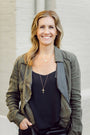 Woman wearing a green jacket and black top with a neutral background