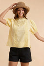 Woman wearing a yellow blouse with lace details and a straw hat on a beige background