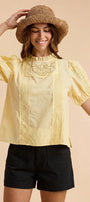Woman wearing a yellow blouse with lace details and a straw hat on a beige background