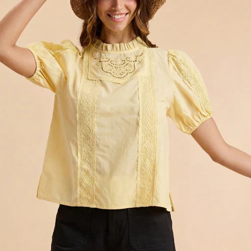 Woman wearing a yellow blouse with lace details and a straw hat on a beige background