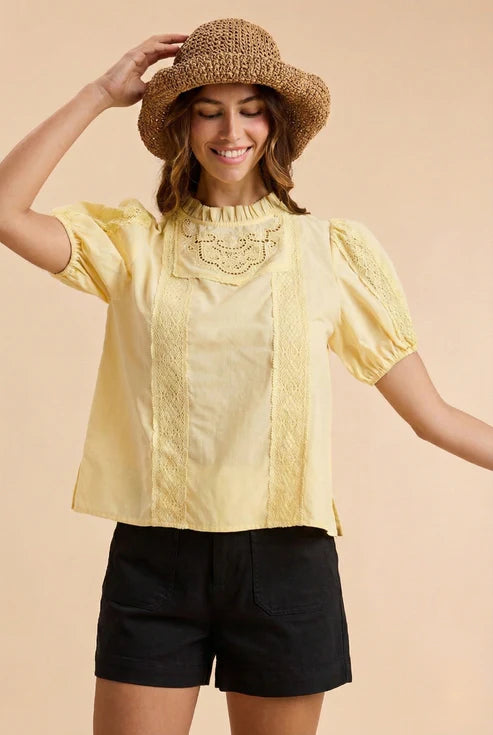 Woman wearing a yellow blouse with lace details and a straw hat on a beige background