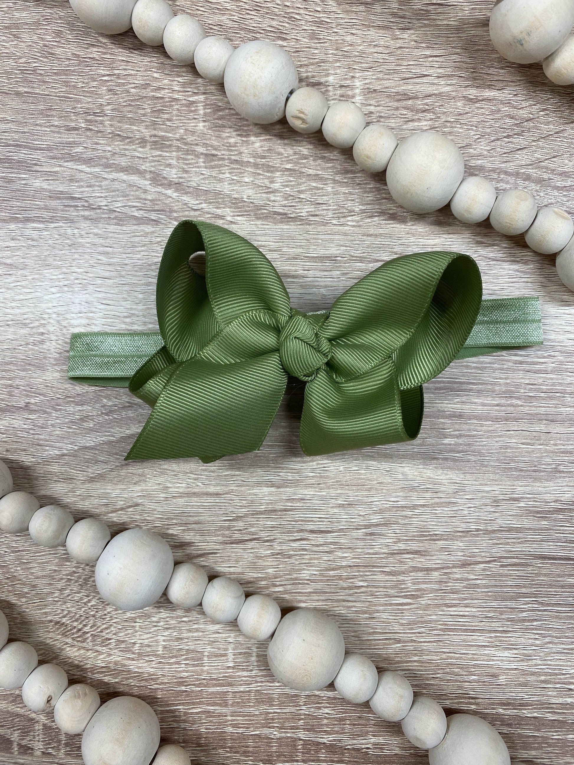 Green hair bow on a wooden surface with white beads