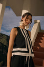 Woman wearing a black and white striped sleeveless top with earrings, standing outdoors.