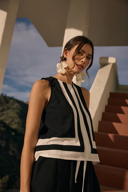 Woman wearing a black and white striped sleeveless top with earrings, standing outdoors.