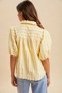 Woman wearing a yellow tie-dye blouse with blue jeans on a beige background