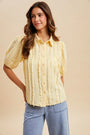 Woman wearing a yellow blouse with ruffled sleeves against a beige background