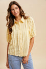 Woman wearing a yellow ruffled blouse and blue jeans against a beige background