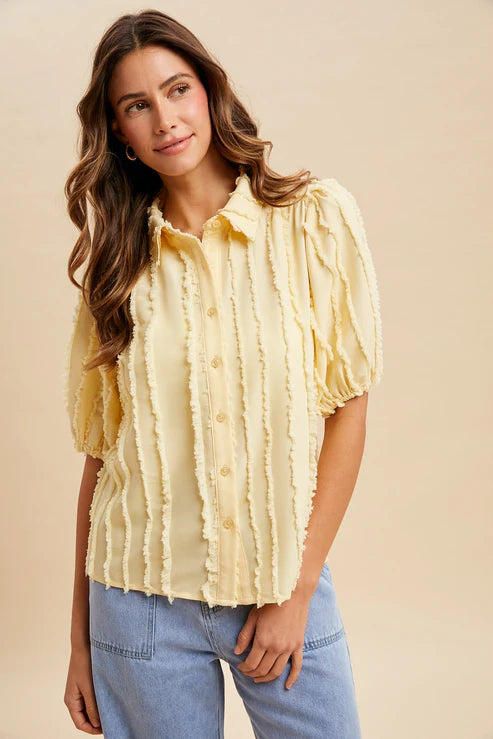 Woman wearing a yellow ruffled blouse and blue jeans against a beige background