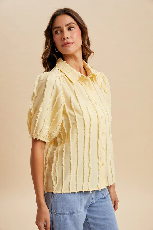 Woman wearing a yellow blouse with ruffled sleeves against a beige background