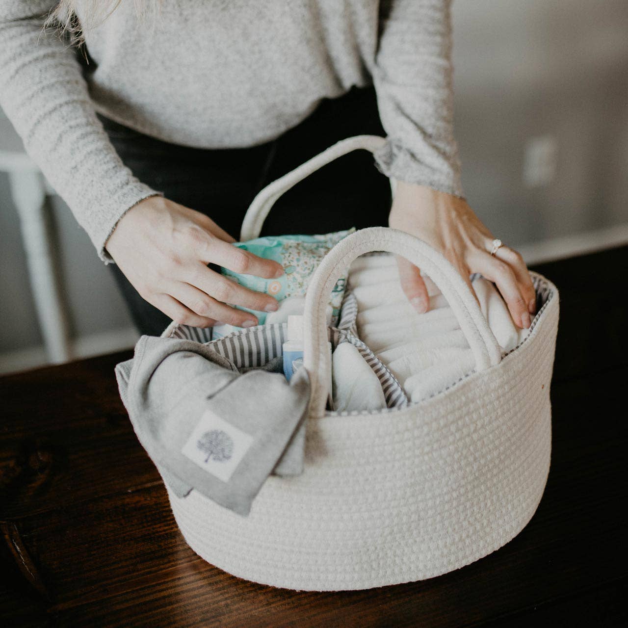 Person holding a basket filled with baby items on a wooden surface