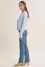 A woman modeling a light blue knit cardigan sweater and blue jeans, shown from a side profile against a plain beige studio background.