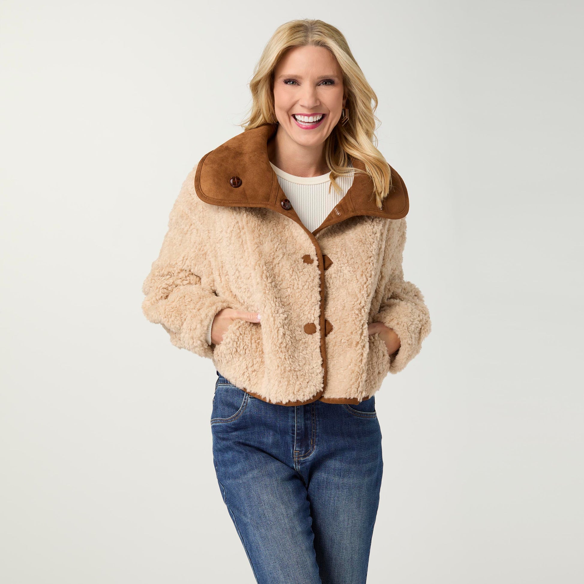 Woman wearing a beige sherpa jacket with brown collar and buttons on a white background