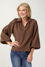 Woman wearing a brown blouse with scalloped hem and blue jeans on a white background