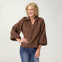 Woman wearing a brown blouse with scalloped hem and blue jeans on a white background
